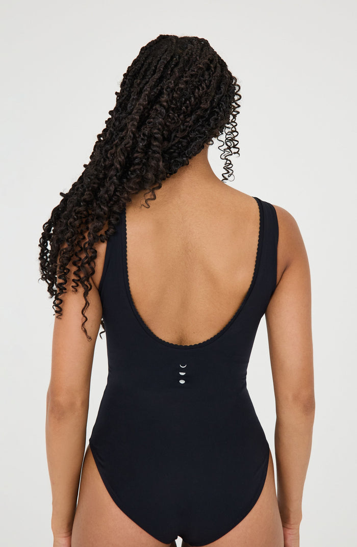 Black one-piece swimsuit with low back and moon phase details, worn by woman with curly hair