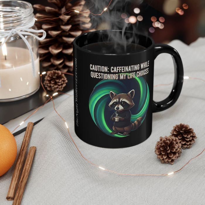 Black mug with a raccoon graphic and text, surrounded by decorative items on a table.