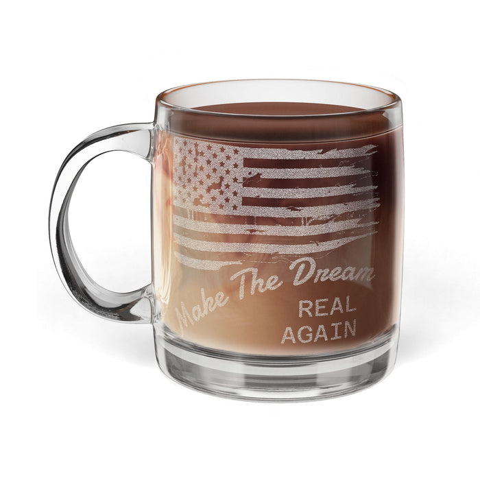 Clear glass mug with American flag design and text 'Make The Dream Real Again' filled with a brown liquid on a white background.