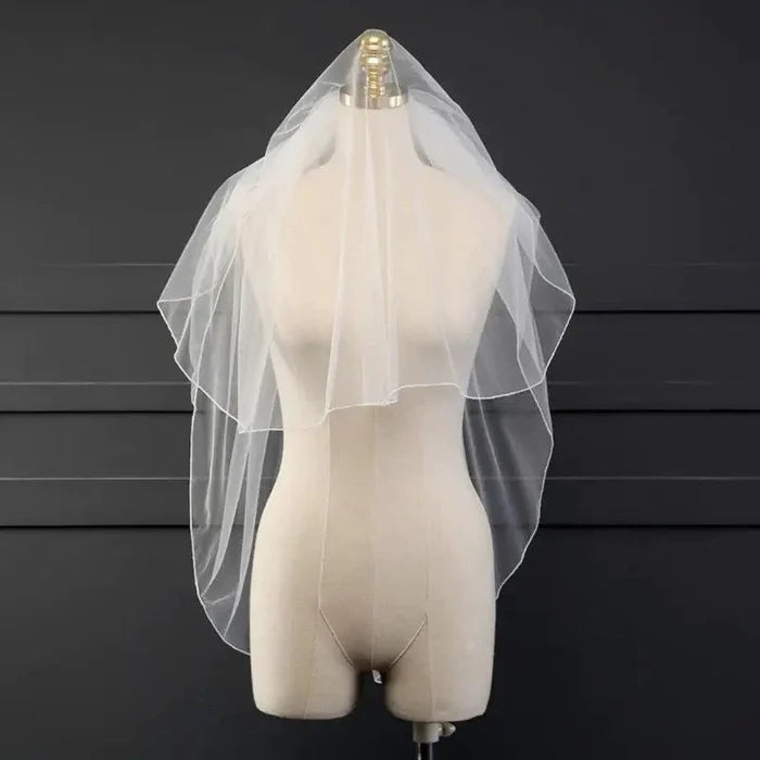 Ethereal double tiered veil by MANDOTOS with delicate lace edging, sheer fabric, and layered design for bridal or special occasion wear.